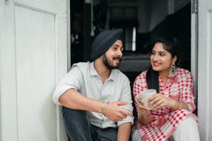 Man and woman sitting in doorway drinking coffee.